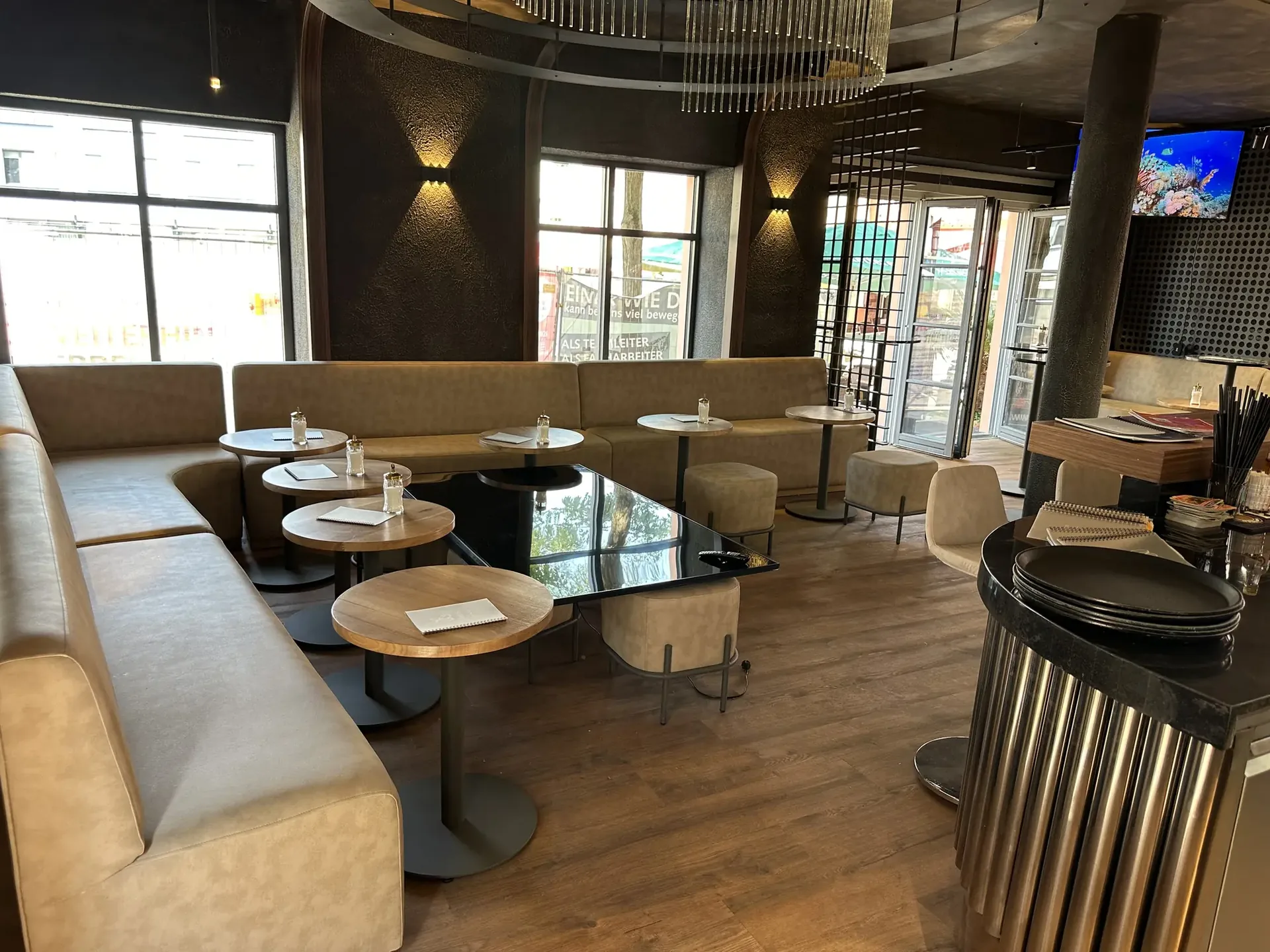 Sitzbereich mit gepolsterten Bankbänken und runden Holztischen in der Café & Bar Zeitlos, im Hintergrund die Theke