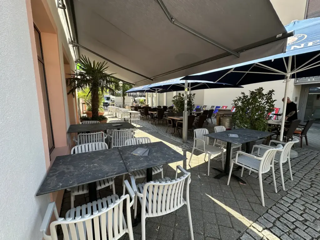 Außenterrasse unter Markise und Sonnenschirmen mit mehreren Sitzgruppen